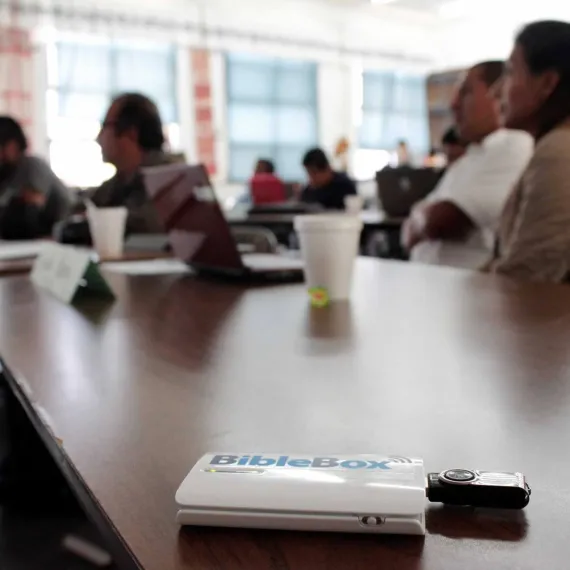 People seated at a conference table with laptops and a notepad in the foreground.