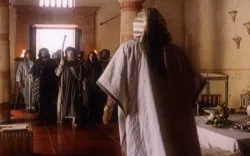 A group of people in robes enters a sunlit room as one person faces them.