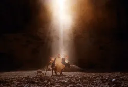 Person with outstretched arms and donkey standing in a spotlight of golden light in a rocky landscape.